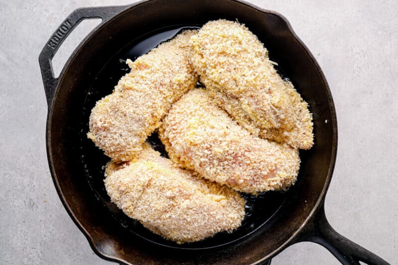 breaded cheesy garlic stuffed chicken breasts in a skillet before cooking