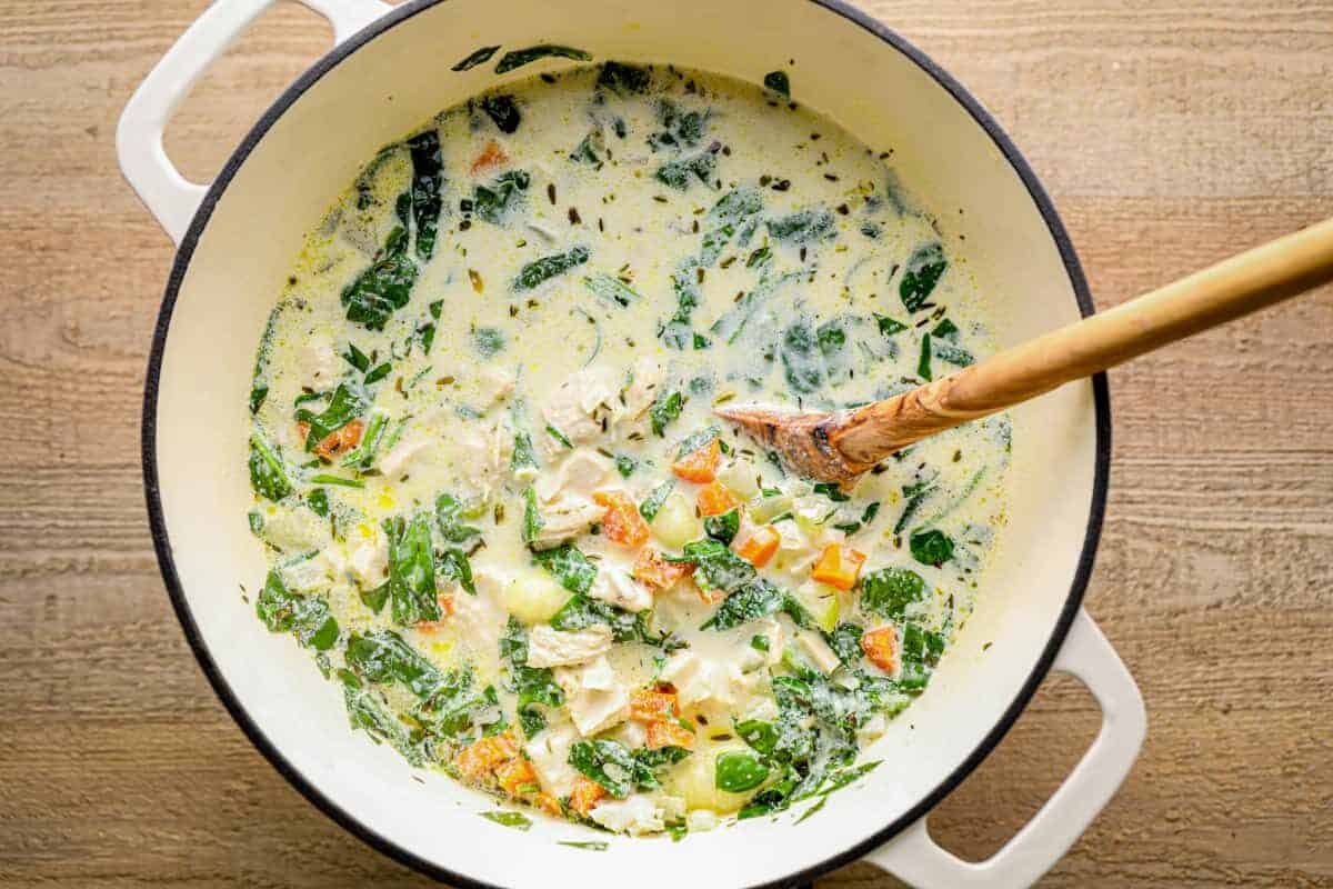 creamy chicken gnocchi soup in a white pot with a wood spoon