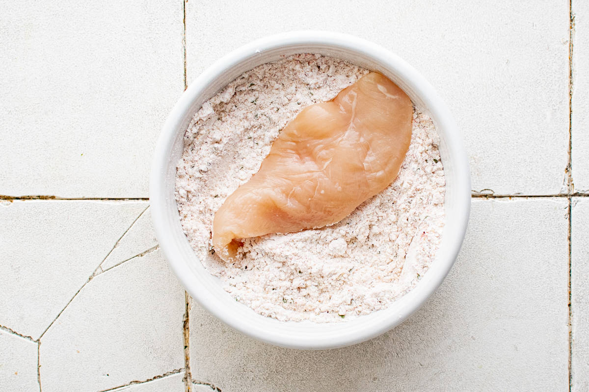 chicken tender in a white bowl with flour and spices mixture.