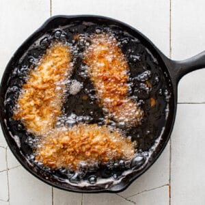 3 pretzel chicken tenders frying in oil in a skillet