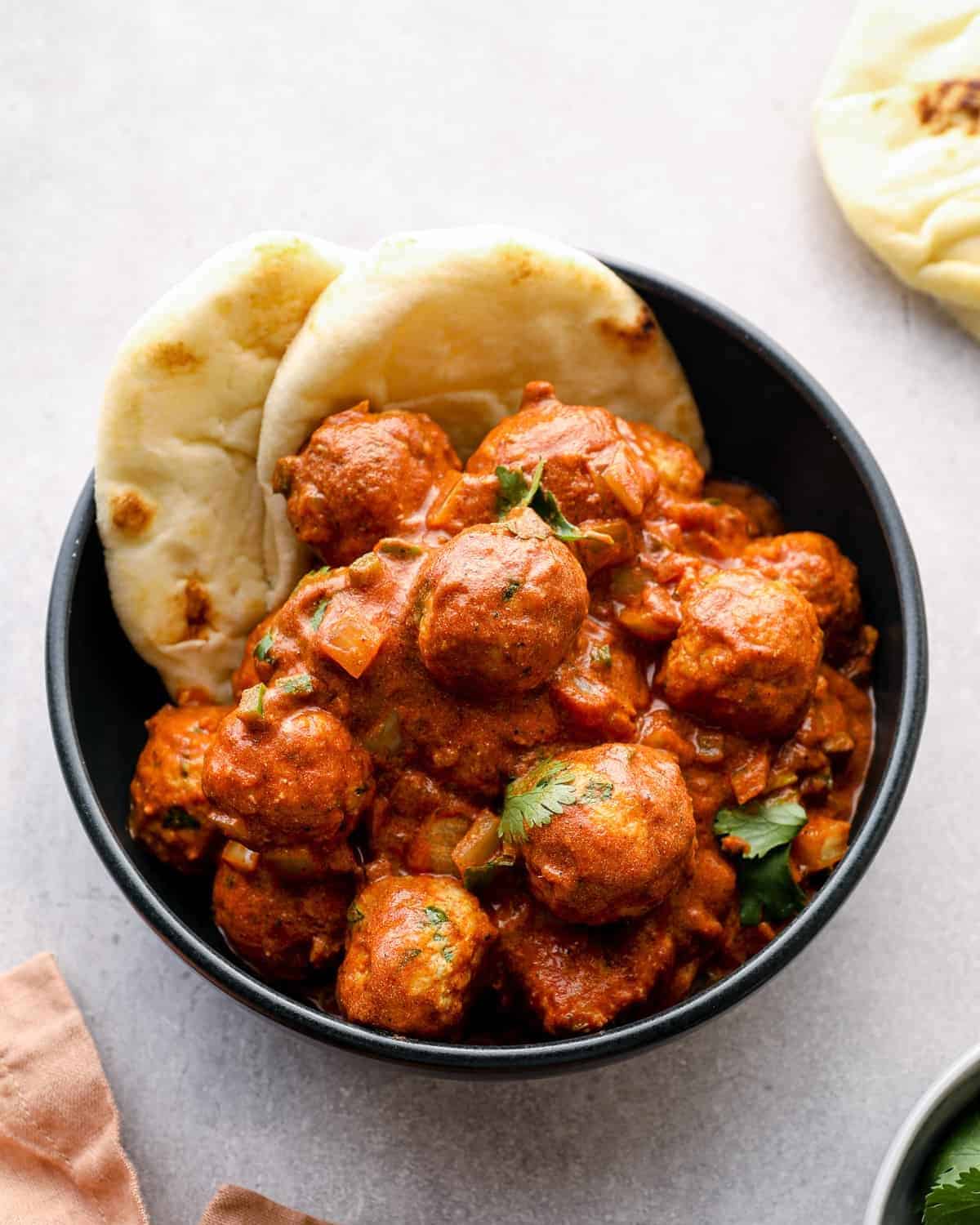 a serving of butter chicken meatballs in a black bowl with naan bread.