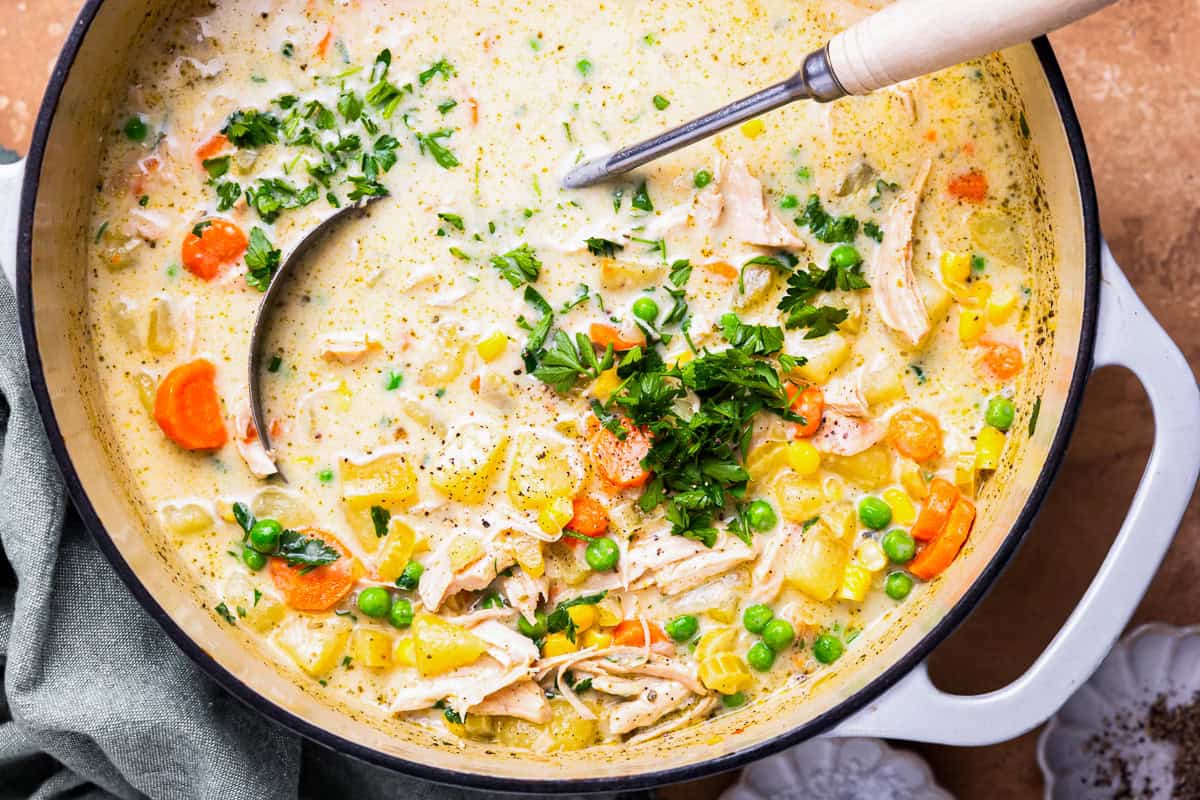 overhead view of a pot of chicken pot pie soup with a ladle and herbs.