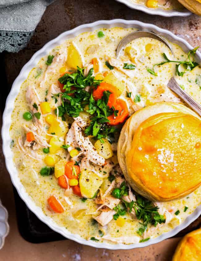 overhead view of a serving of chicken pot pie soup in a bowl with a biscuit.