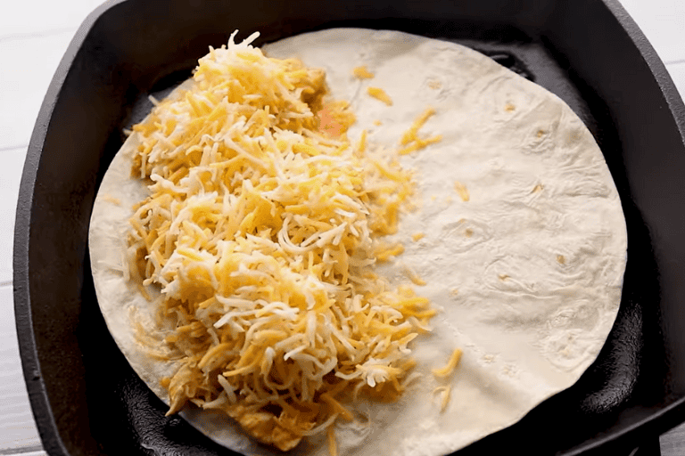 Buffalo chicken and shredded cheese covering half of a tortilla.