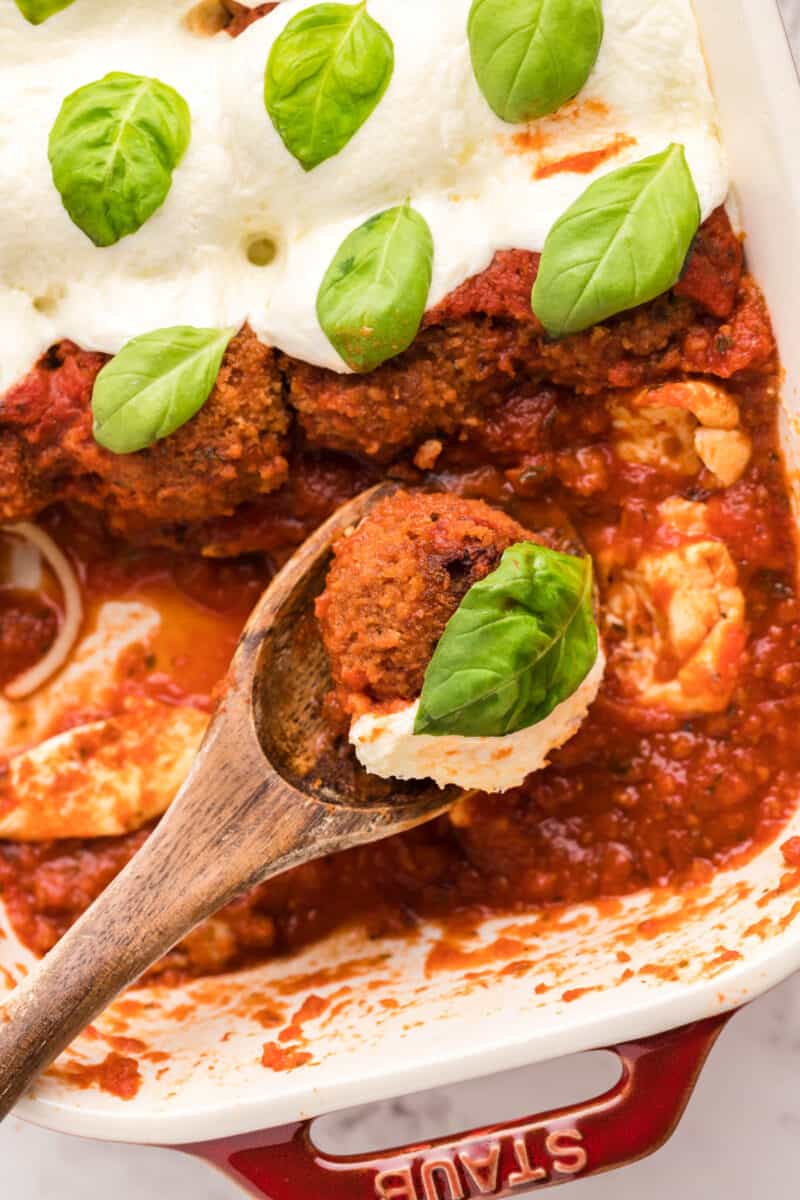 wood spoon held over a baking dish filled with chicken parmesan meatballs with one meatball on the spoon