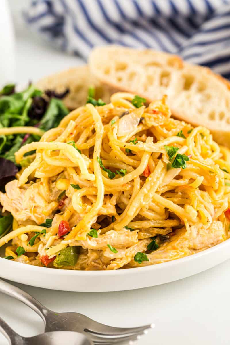 chicken spaghetti casserole on a white plate with bread and salad