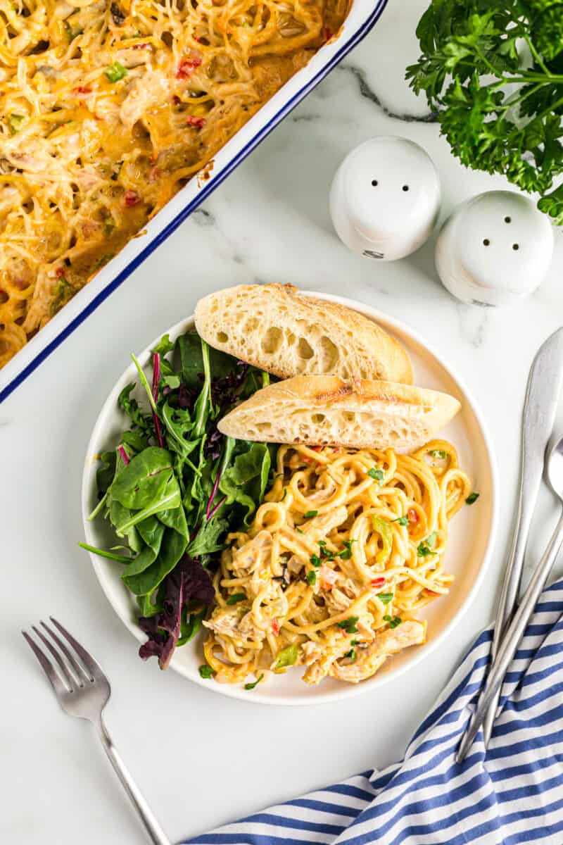 overhead image of chicken spaghetti casserole on a white plate with bread and salad