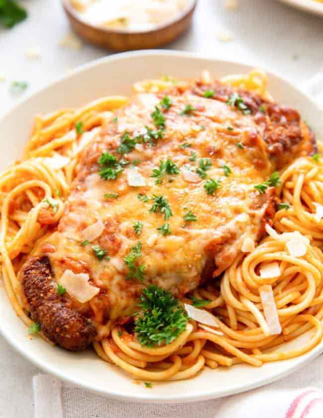 chicken parmesan on top of spaghetti on a white plate