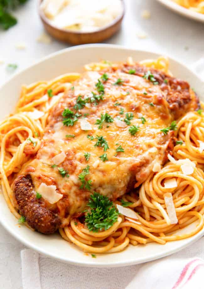 chicken parmesan on top of spaghetti on a white plate