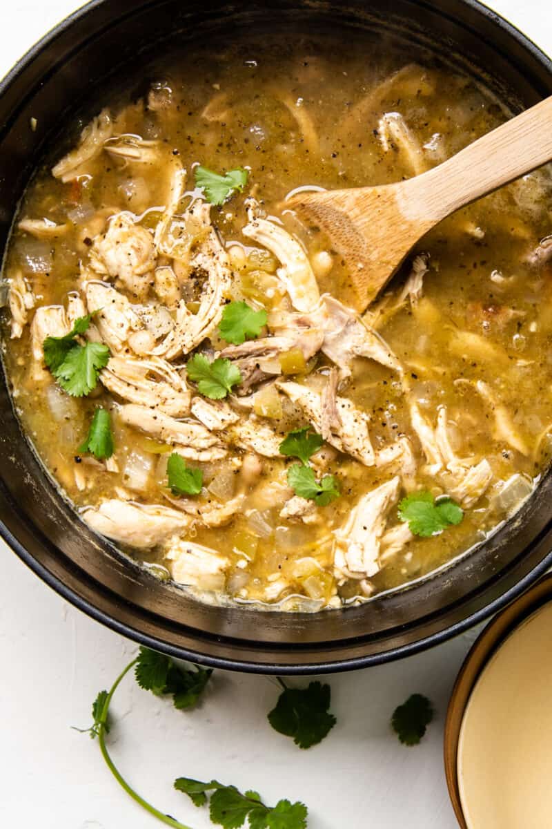 green chile chicken soup in a pot with a wood spoon