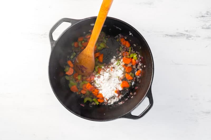 flour added to sautéed veggies in a pot with a wood spoon
