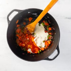 Buffalo sauce and ranch dressing added to sautéed veggies in a pot with a wood spoon