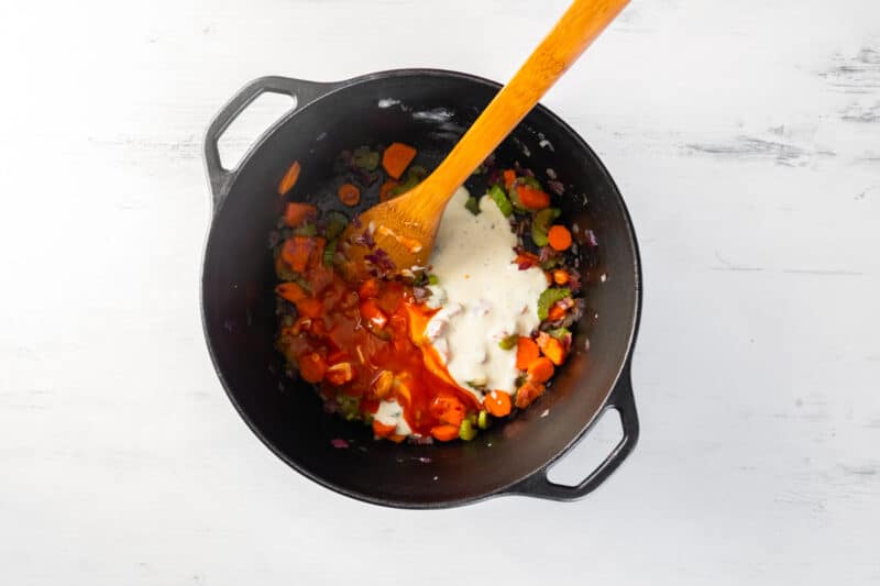 Buffalo sauce and ranch dressing added to sautéed veggies in a pot with a wood spoon