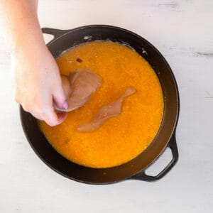 hand placing chicken breasts in a pot of soup