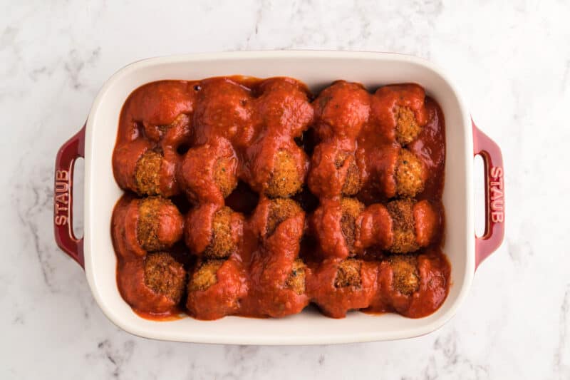 chicken parmesan meatballs in a baking dish topped with marinara sauce