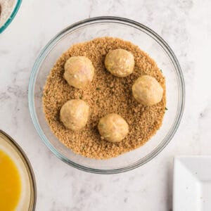 5 chicken meatballs coated in flour and eggs in a bowl of seasoned breadcrumbs