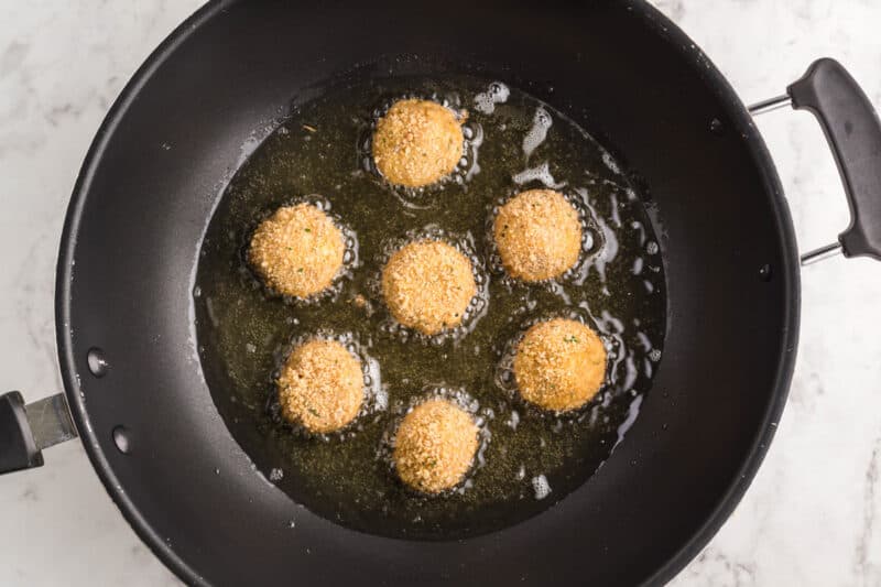 7 chicken meatballs frying in a skillet