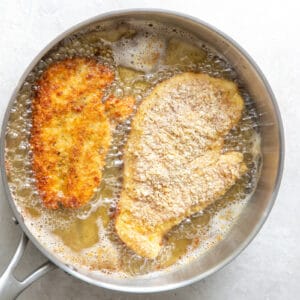 2 chicken breasts frying in a pan of oil