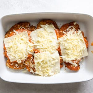 fried chicken breasts topped with sauce and cheese in a baking dish