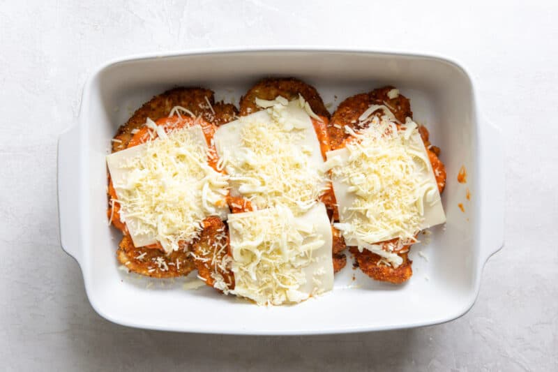 fried chicken breasts topped with sauce and cheese in a baking dish