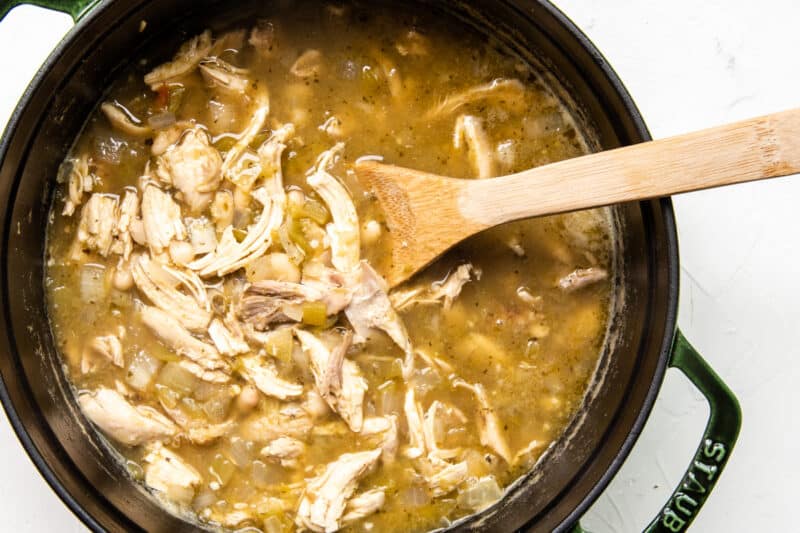 chicken, broth, and veggies added to pot with a wood spoon
