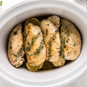 browned chicken breasts topped with thyme sprigs in a crockpot