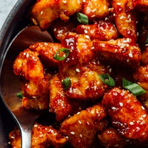korean fried chicken with a serving spoon in a black bowl