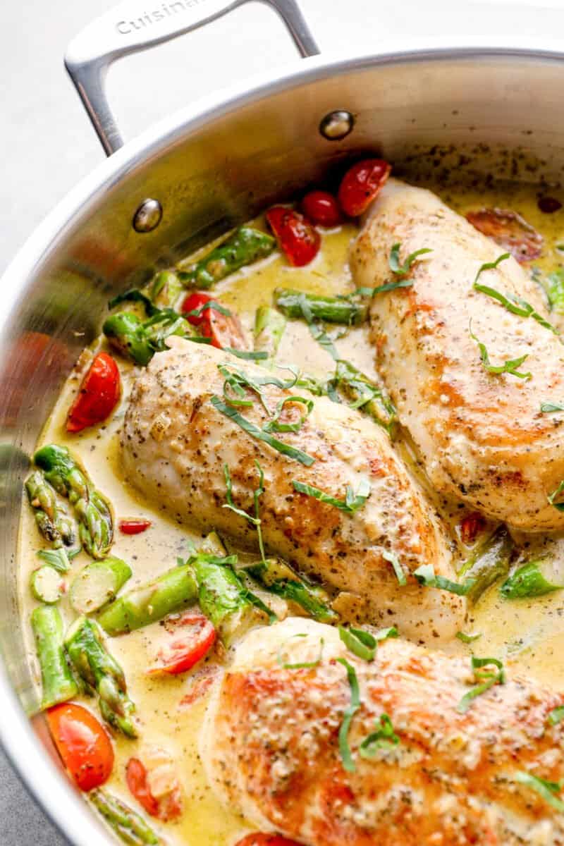 chicken breasts in a skillet with pesto cream sauce, tomatoes, and asparagus
