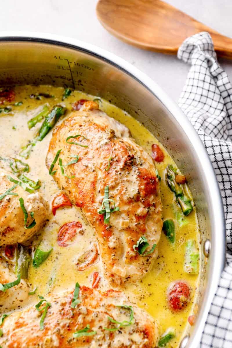chicken breast in a skillet with pesto cream sauce, tomatoes, and asparagus