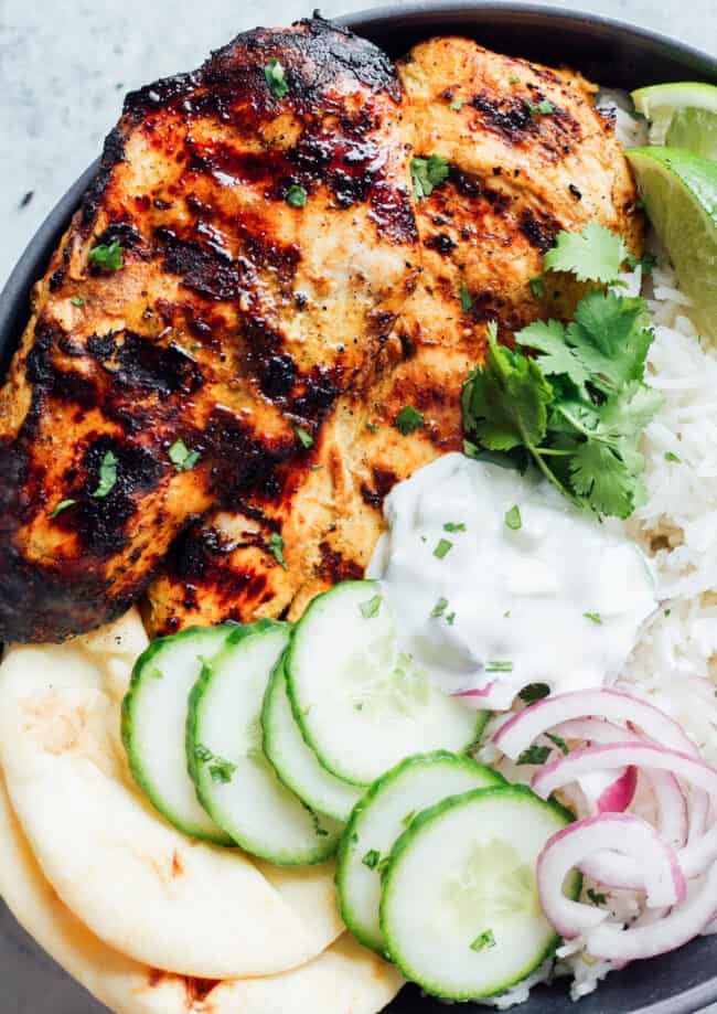grilled tandoori chicken breast on a gray plate with cucumbers, onions, naan bread, and rice