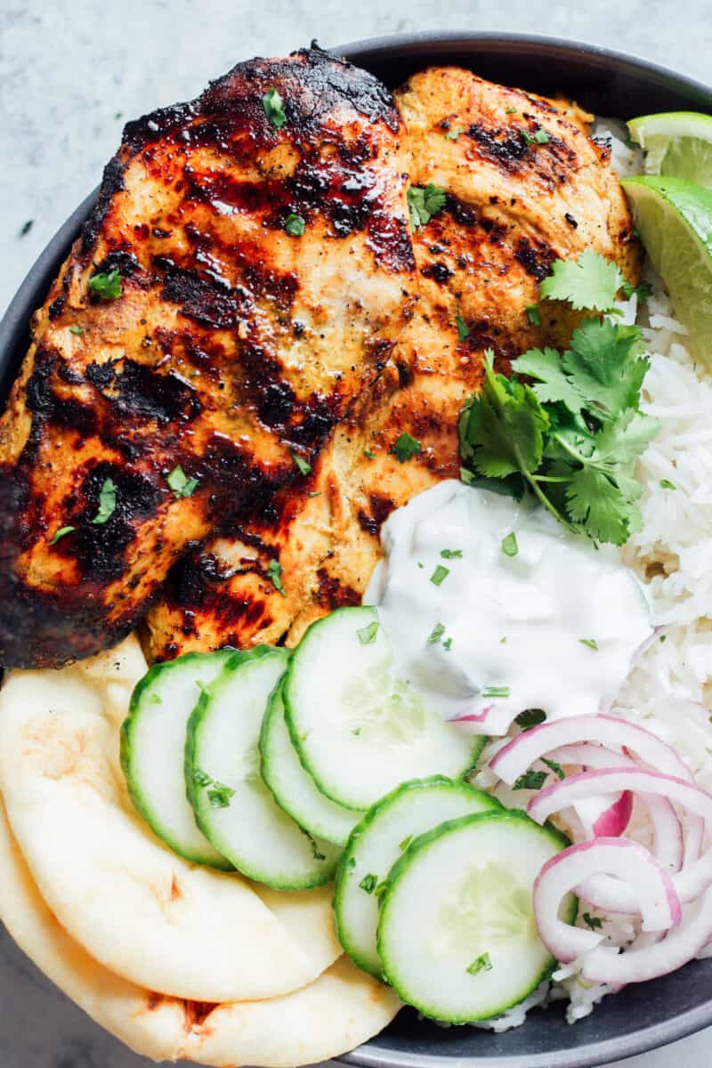 grilled tandoori chicken breast on a gray plate with cucumbers, onions, naan bread, and rice