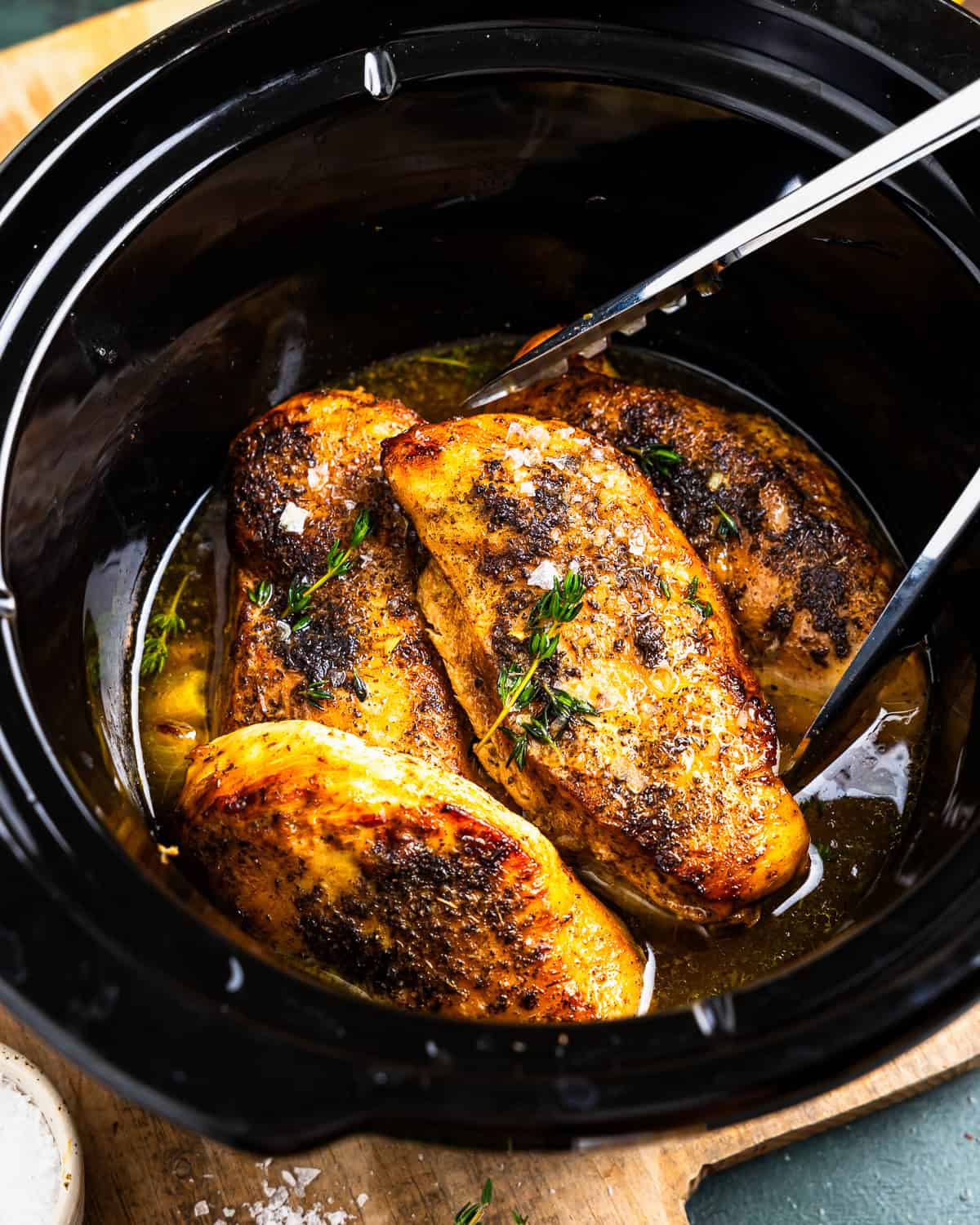 crockpot lemon chicken in a slow cooker with tongs.