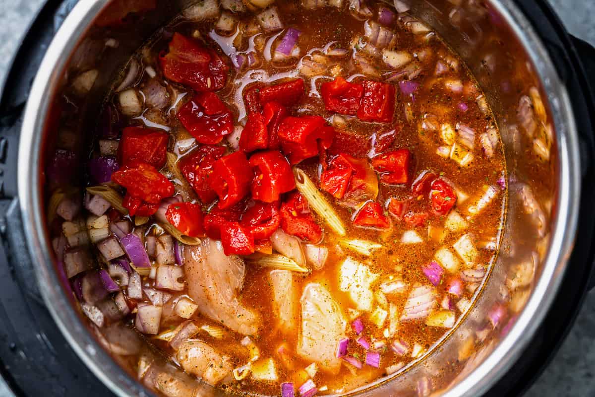 diced tomatoes over chicken in seasoned broth with vegetables in an instant pot.