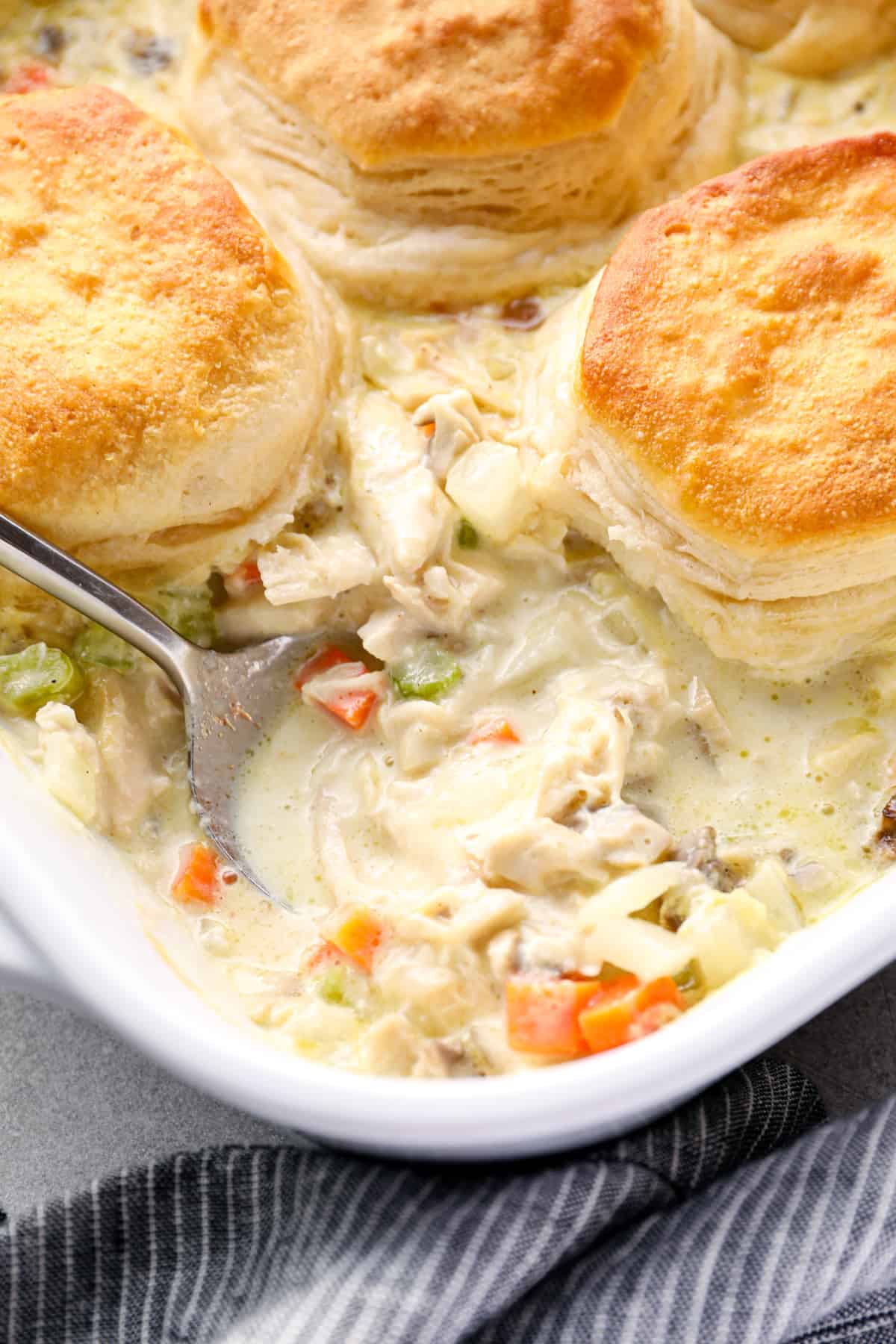 chicken pot pie casserole topped with biscuits in a white baking dish with a spoon