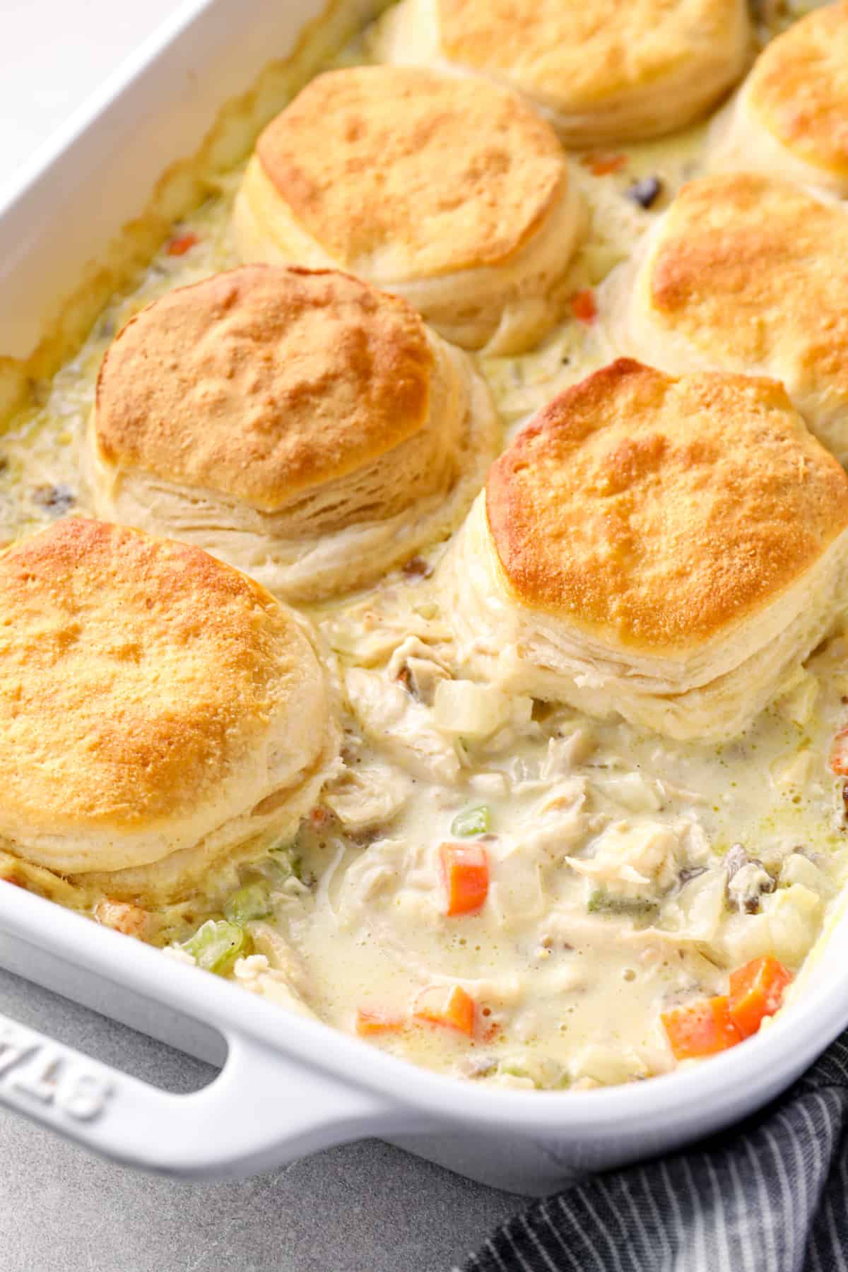 chicken pot pie casserole topped with biscuits in a white baking dish