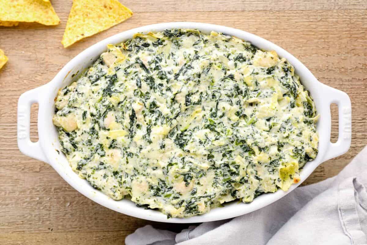 overhead image of chicken spinach artichoke dip in a white baking dish after baking