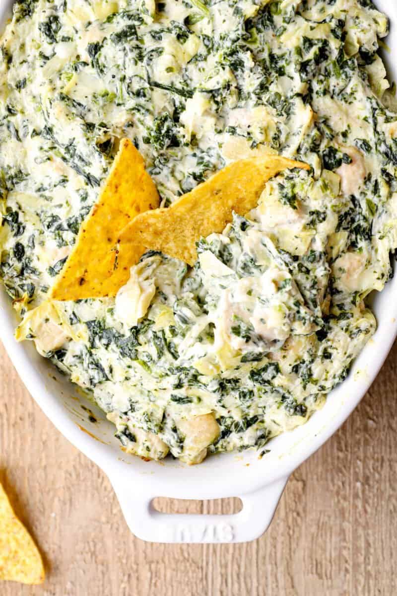 overhead image of chicken spinach artichoke dip in a white baking dish with tortilla chips