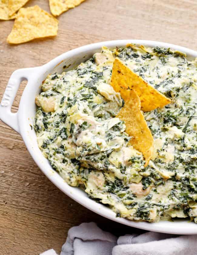 chicken spinach artichoke dip in a white baking dish with tortilla chips