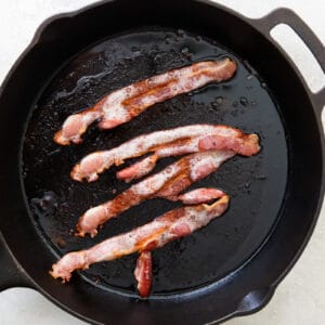 bacon strips cooking in a cast iron skillet