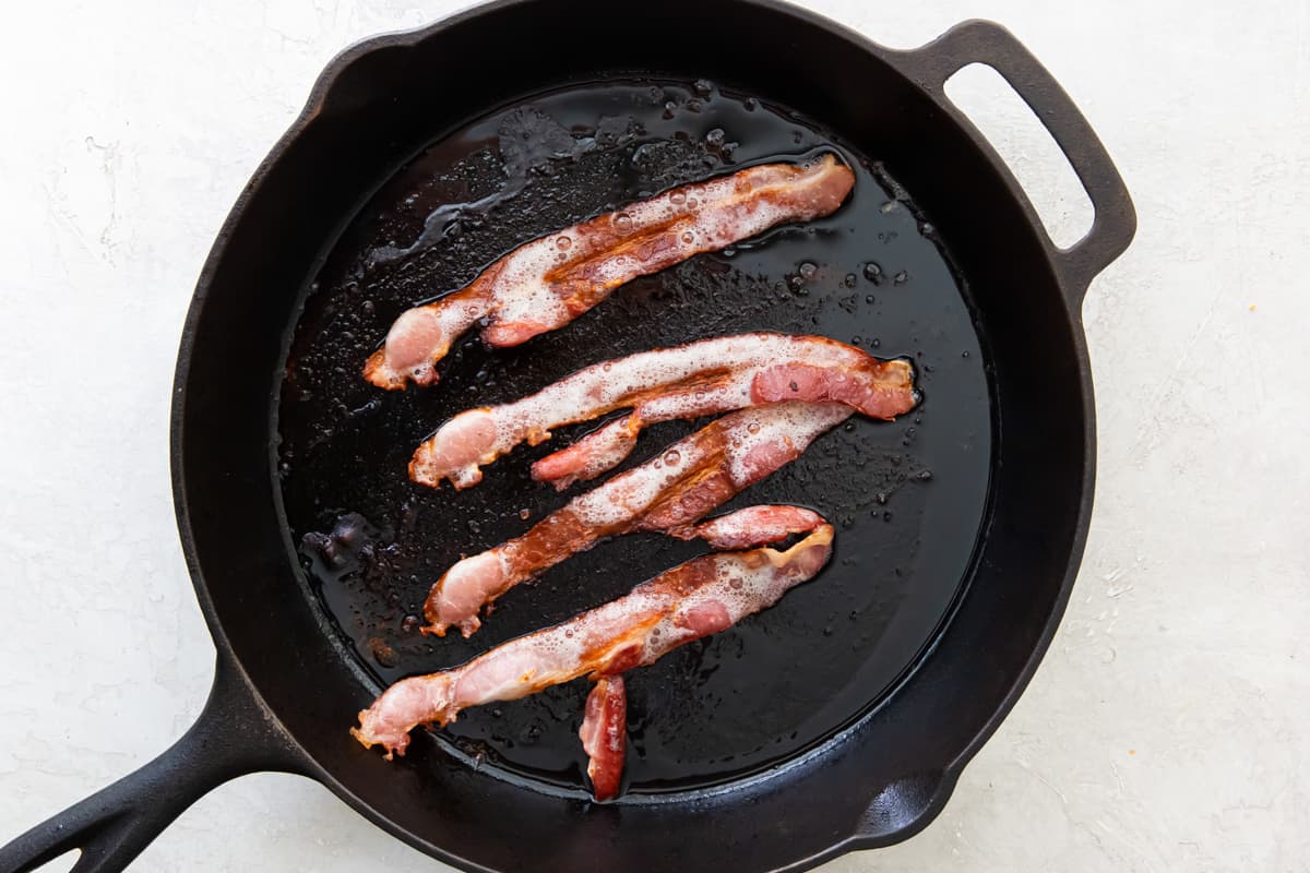 Bacon strips cooking in a cast iron skillet