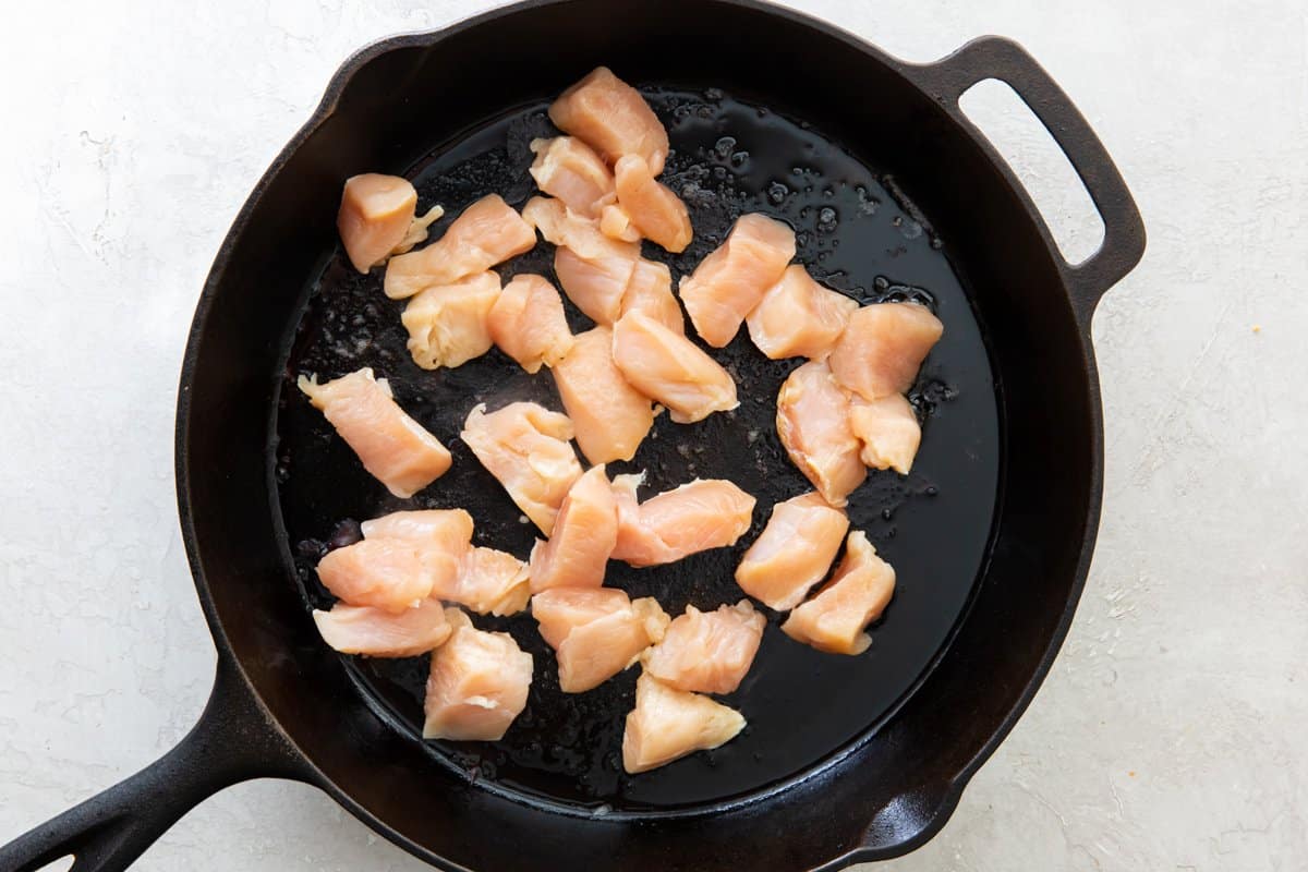 Pieces of chicken cooking in a skillet.