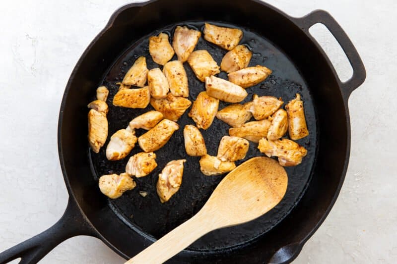 cooked chicken in a skillet with a wood spoon