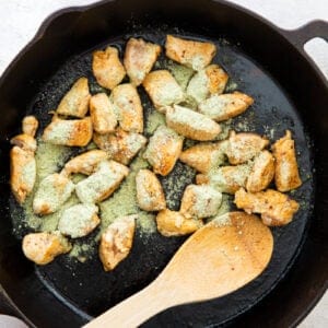 ranch seasoning mix added to cooked chicken in a skillet with a wood spoon