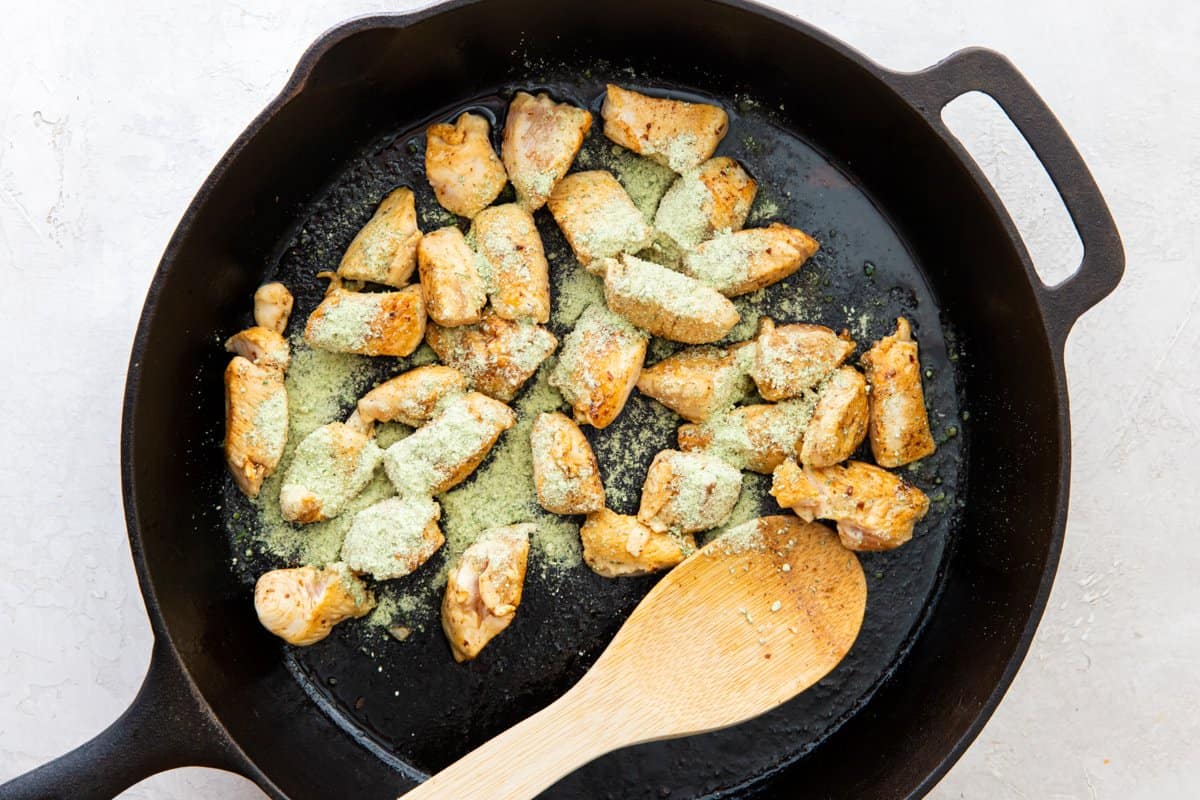 Browned pieces of chicken in a skillet, covered in ranch seasoning mix.
