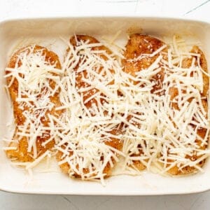 seasoned chicken breasts in a baking dish topped with shredded cheese