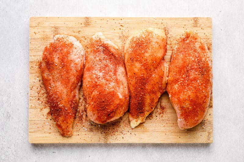 seasoned raw chicken breasts on a wood cutting board