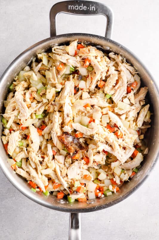 shredded chicken added to chopped vegetable filling in a pan