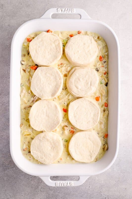 chicken pot pie casserole topped with biscuits in a white baking dish before baking