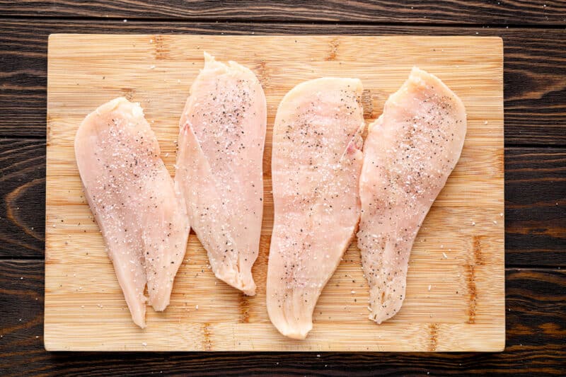 raw chicken breasts on a cutting board seasoned with salt and pepper