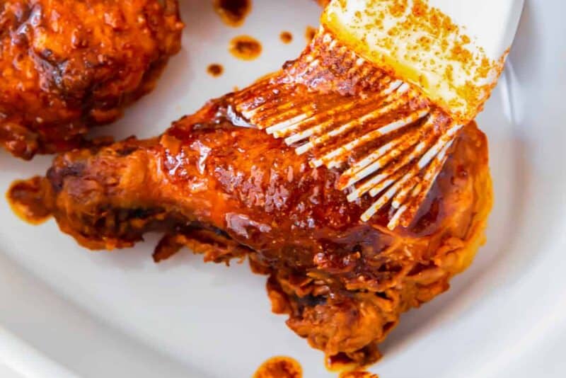 brushing hot sauce onto pieces of fried chicken on a white platter